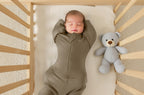 Baby in a green onesie lying in a crib with a gray teddy bear